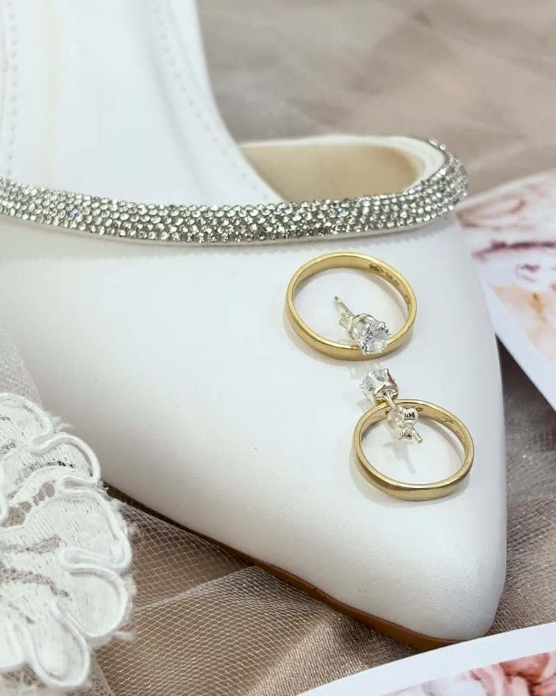 Alianças sobre o sapato da noiva, ao lado de renda branca